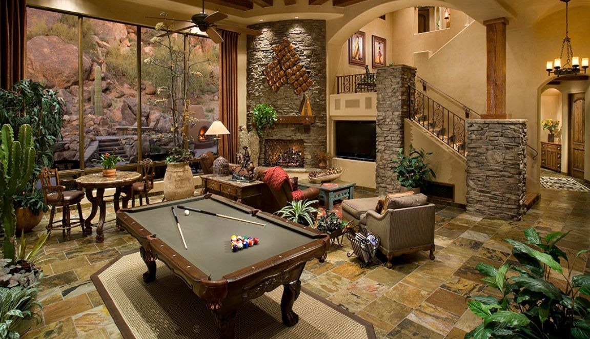 Spanish Mediterranean game room with billiards table, stone fireplace, tall windows and desert boulder views